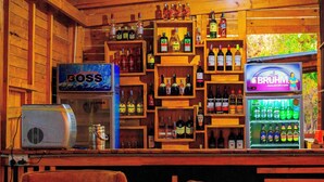 Zona de bar con estantes llenos de botellas de licor, un letrero que dice 'Boss', un letrero que dice 'Bruhm' y un refrigerador repleto de bebidas.