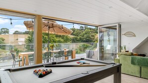 A pool table in a modern room with large windows, a dining area, and a green sofa. - Sea Holly House in Beer (Seaton)