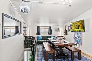 A modern dining area with a long wooden table, black and white patterned rug, and a large window with curtains. - Denver Group Compound: Sleeps 30! Game Rooms, Hot Tub, Private Chef + ShuttleVan (Denver)