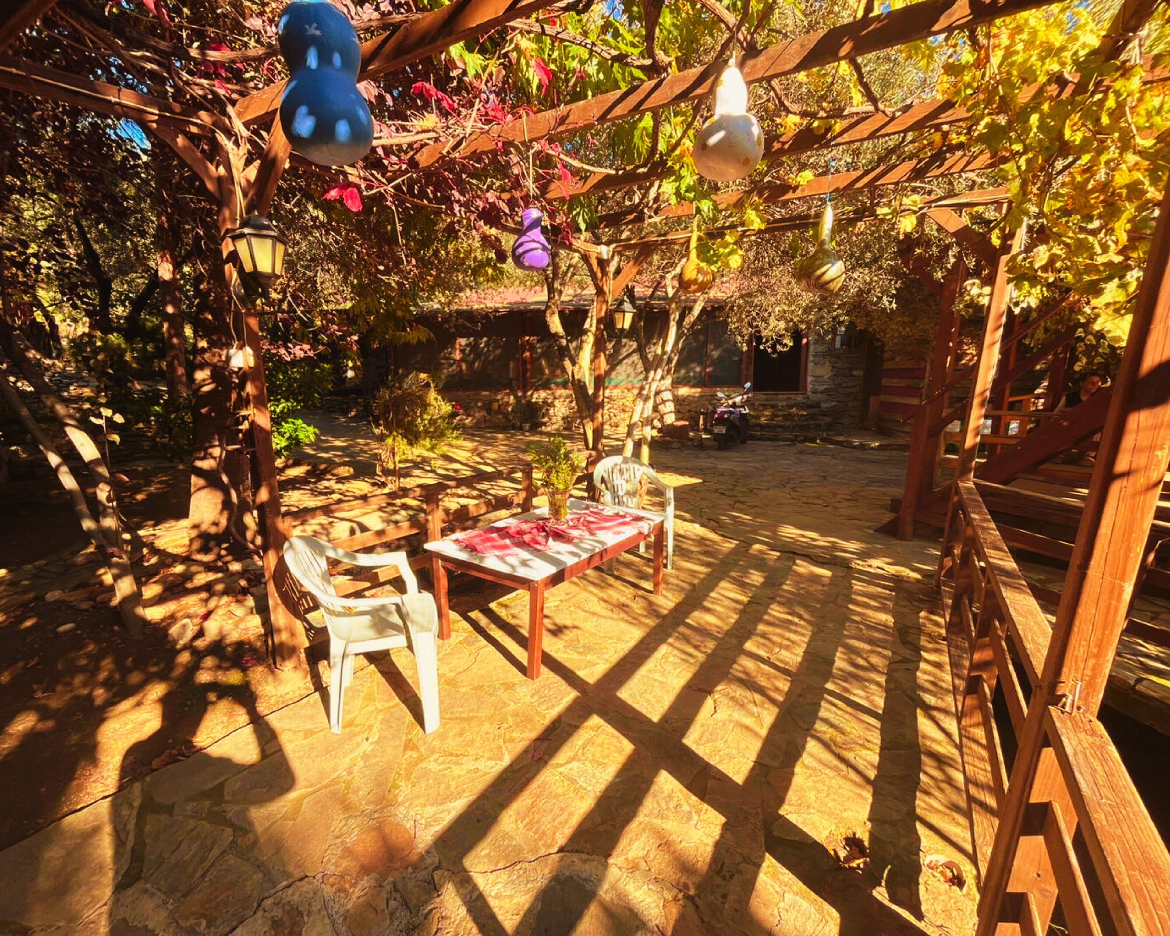 An outdoor patio with stone flooring, wooden furniture, and hanging light fixtures.