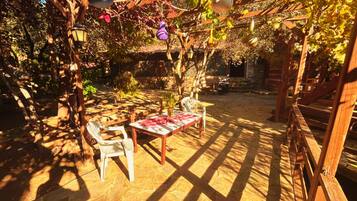 An outdoor patio with stone flooring, wooden furniture, and hanging light fixtures.