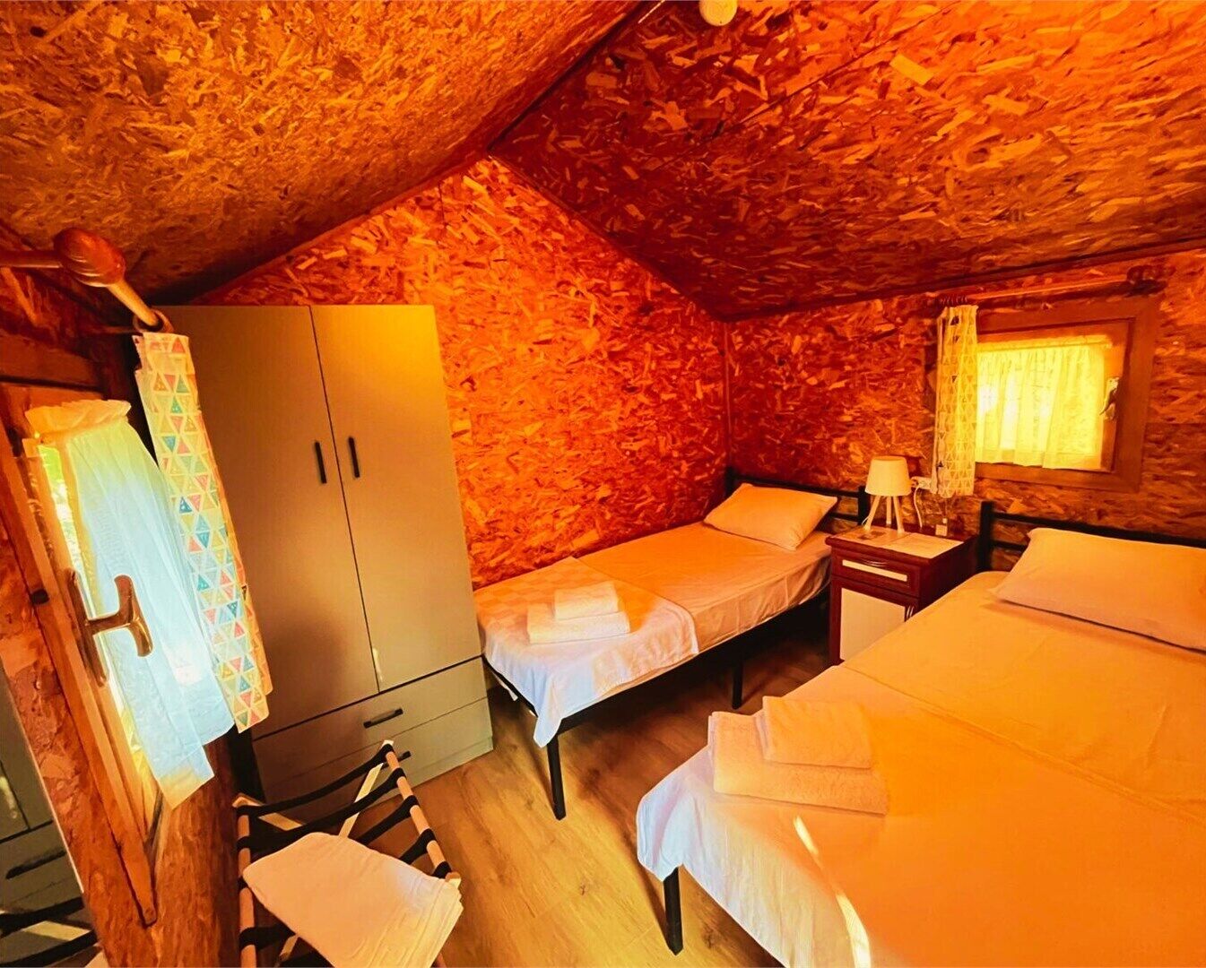 Une chambre mansardée chaleureuse, avec deux lits simples, une armoire en bois et une petite table avec une lampe.