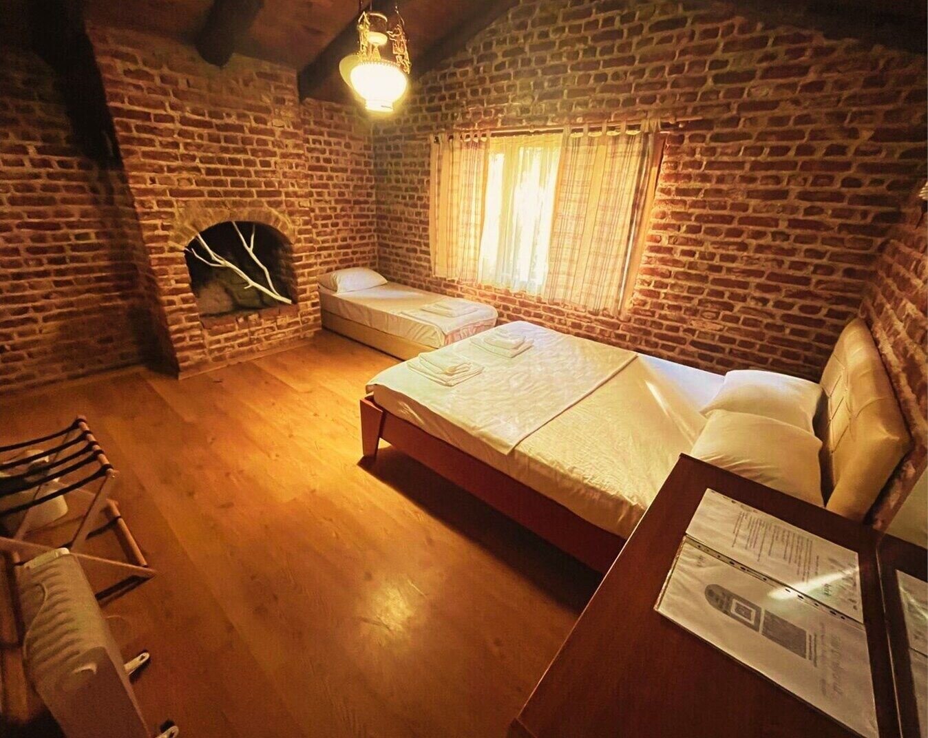 A cozy room with a brick wall, a wooden floor, a bed, a chair, and a hanging light fixture.