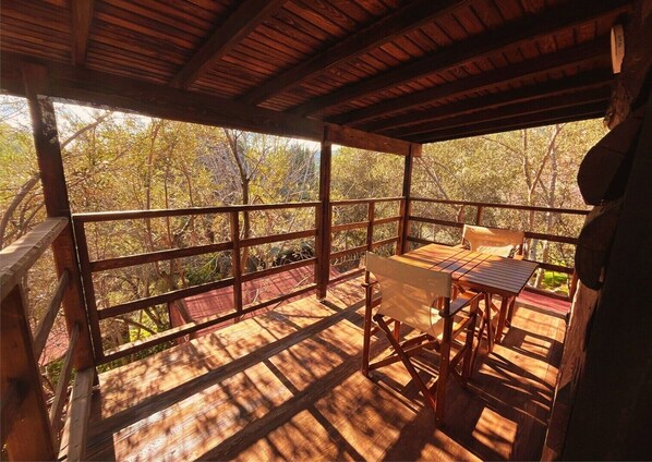 A wooden deck with a table and chairs, surrounded by a wooden railing, overlooking a forested area. - Kybele Nature Life (Edremit)