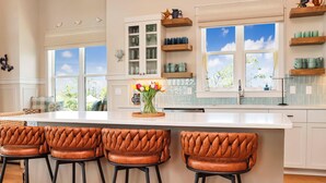 A kitchen with a large island, bar stools, and a window with a view of greenery. - Villa Laguna (Port St. Joe)