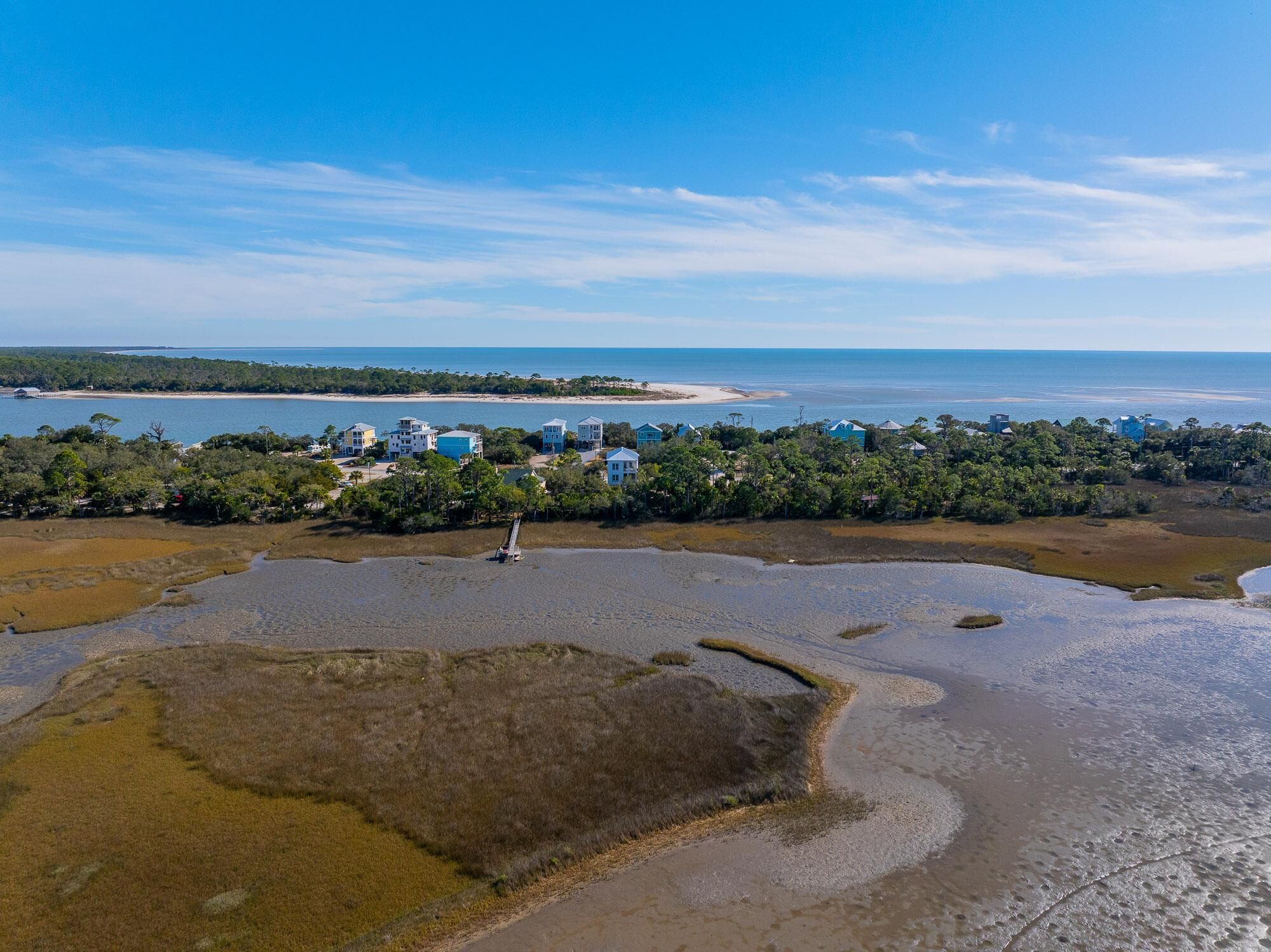 Vista aérea de una zona costera con playa, casas y un muelle.