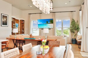 A spacious living room with a wooden dining table, a sofa, and a TV displaying a beach scene. - Villa Laguna (Port St. Joe)