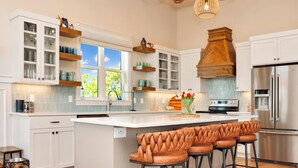 A modern kitchen with white cabinets, a central island with bar stools, and a stainless steel refrigerator. - Villa Laguna (Port St. Joe)
