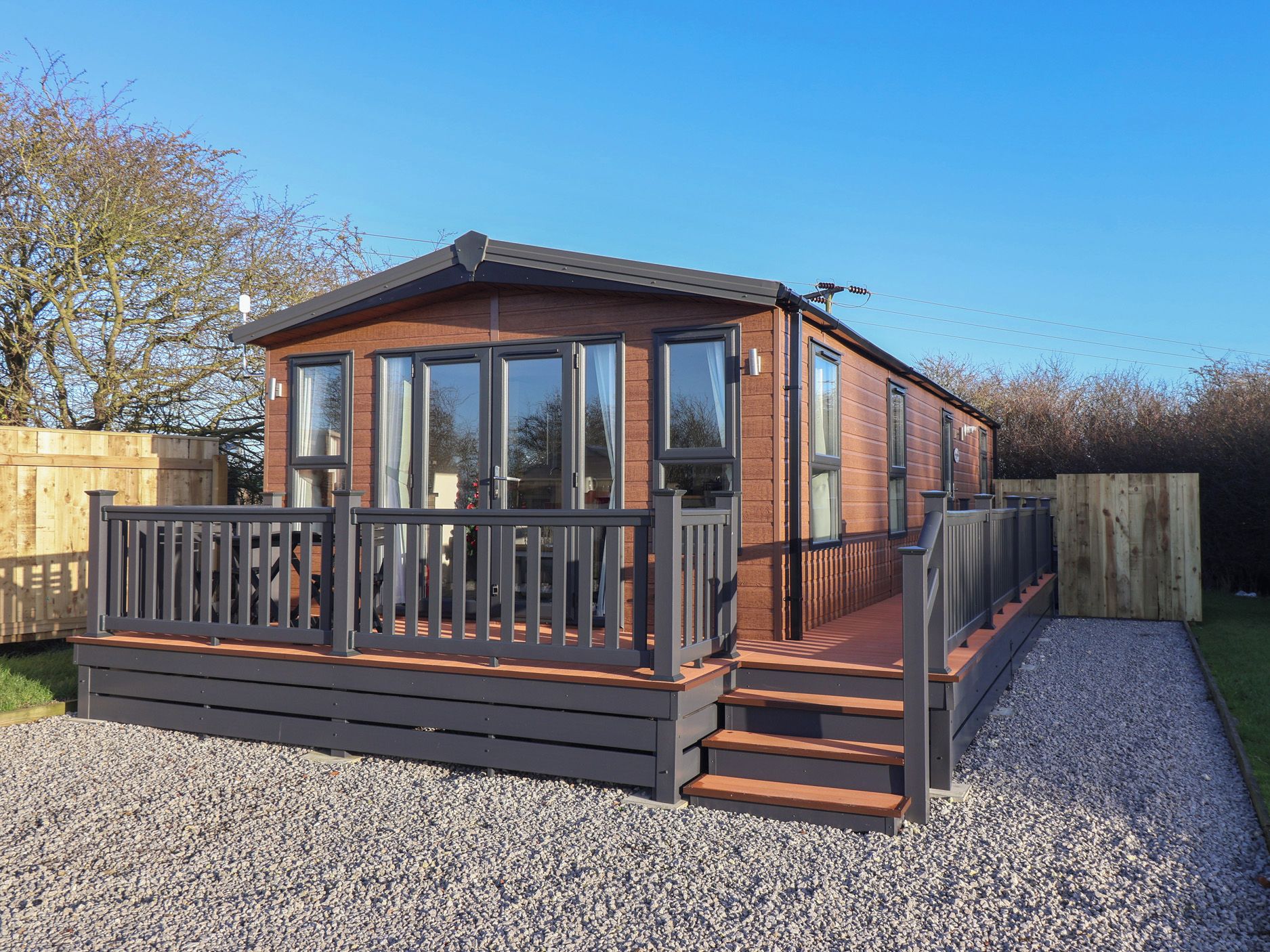 Une cabane en bois dotée de grandes fenêtres, d’une terrasse et d’une allée gravillonnée.