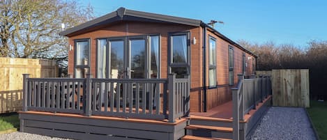 A wooden cabin with large windows, a deck, and a gravel driveway.