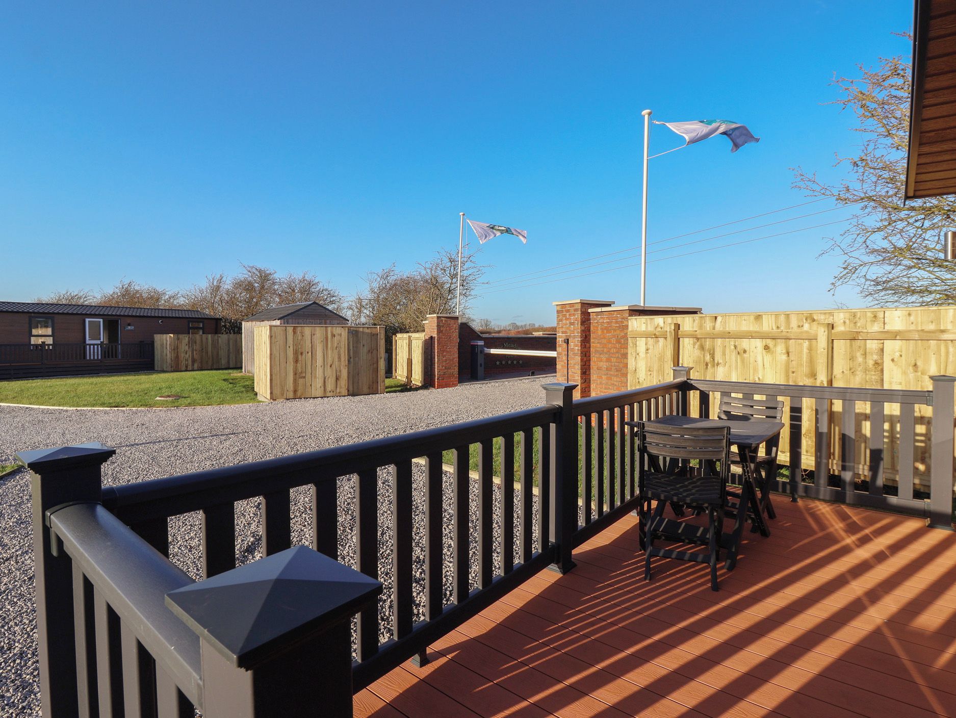 A deck with a table and chairs, a wooden fence, and a flagpole with flags.