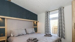 A bedroom with a bed, wooden headboard, and a window with patterned curtains.