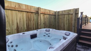 A hot tub adjacent to a wooden fence with a wooden deck and stairs leading up to a covered area.