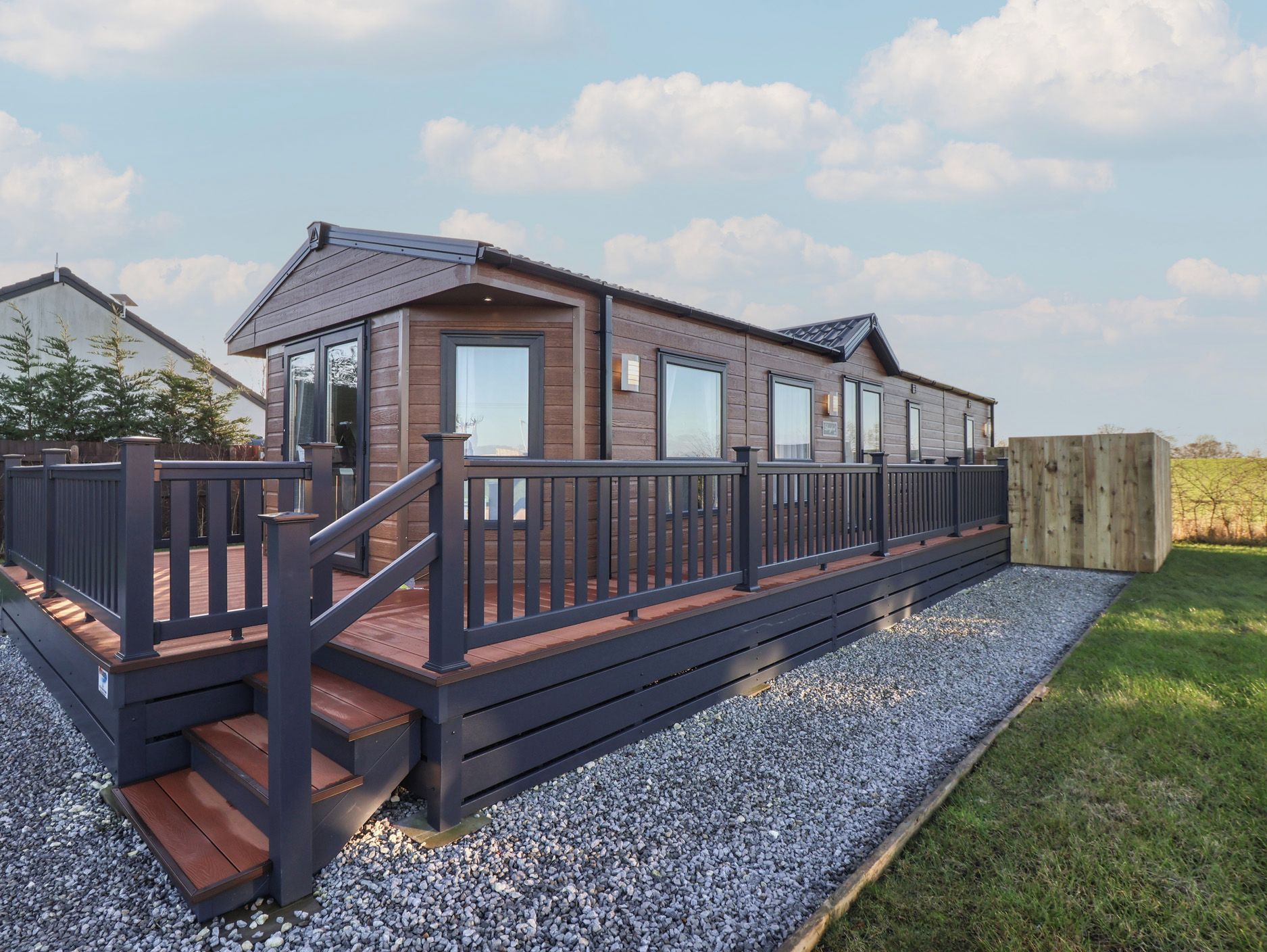 Une maison mobile moderne dotée d’une terrasse en bois et d’un chemin en gravier.