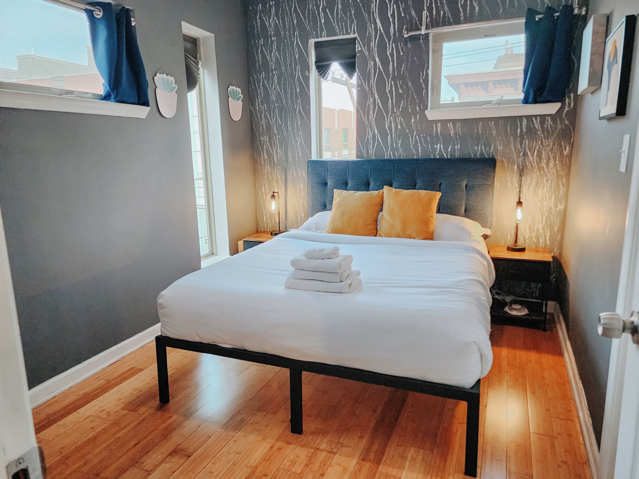A neatly made bed with white linens and two pillows, a bedside table with a lamp, and a window with curtains.