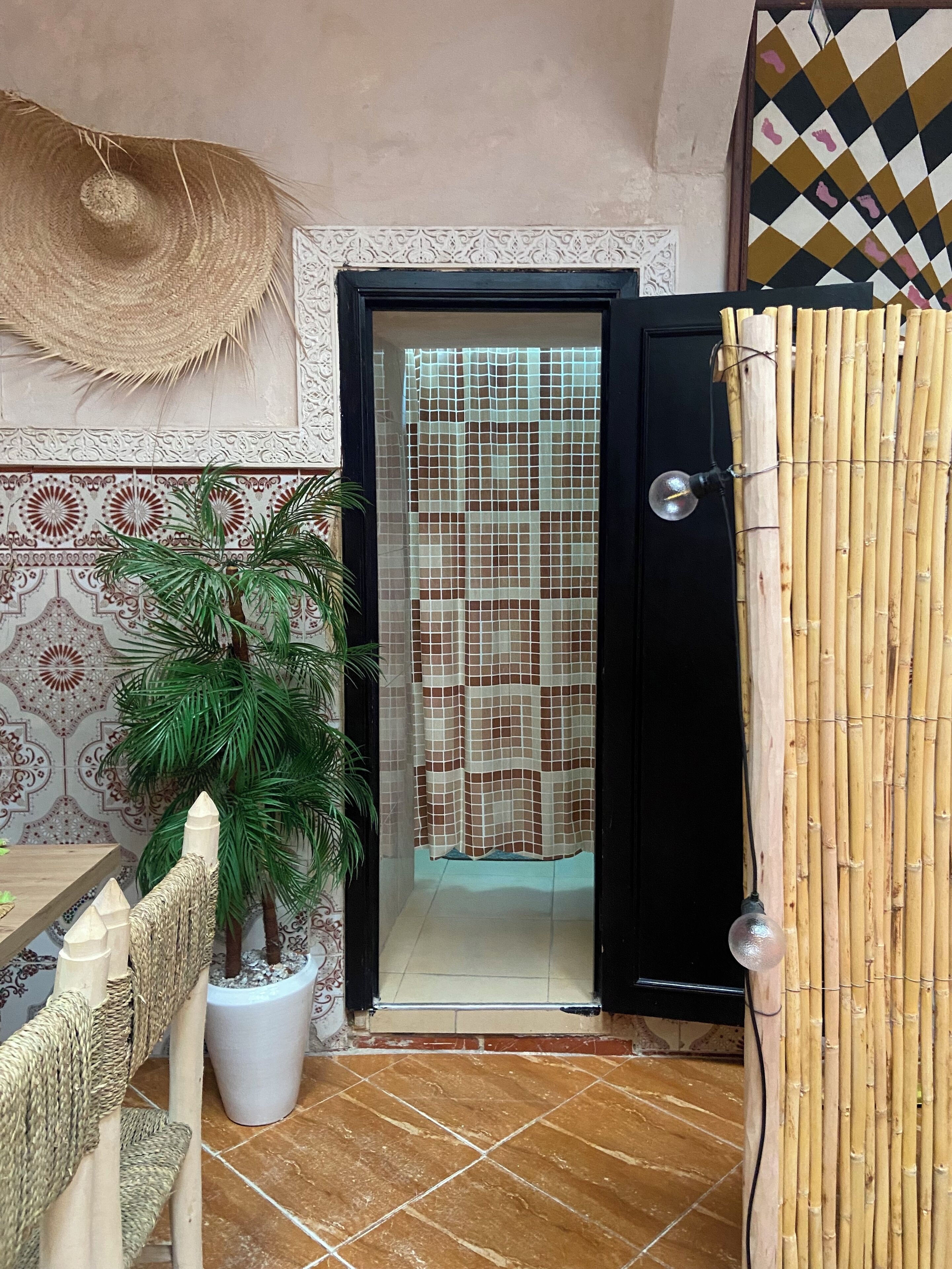 A room with a tiled floor, a door with a patterned curtain, a woven chair, and a potted plant.