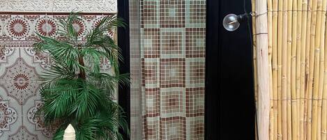 A room with a tiled floor, a door with a patterned curtain, a woven chair, and a potted plant.