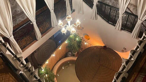 Un espacio circular con hidromasaje, cortinas blancas, una araña y un banco de madera.