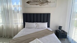 A bedroom with a large bed, a headboard, a wall-mounted feather artwork, a bedside table with a lamp, and sheer curtains. - Luxurious Motherland Apartments (Lusaka)