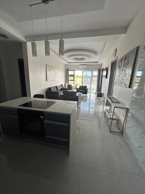 A modern kitchen with a central island, a dining area with a sofa and chairs, and a living room with a TV and artwork. - Luxurious Motherland Apartments (Lusaka)