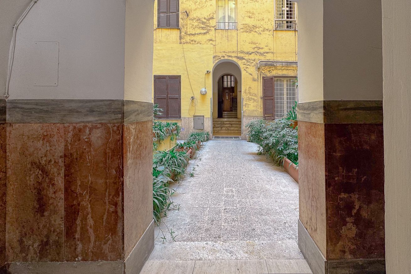 A narrow alleyway with a yellow building, a door, and potted plants.