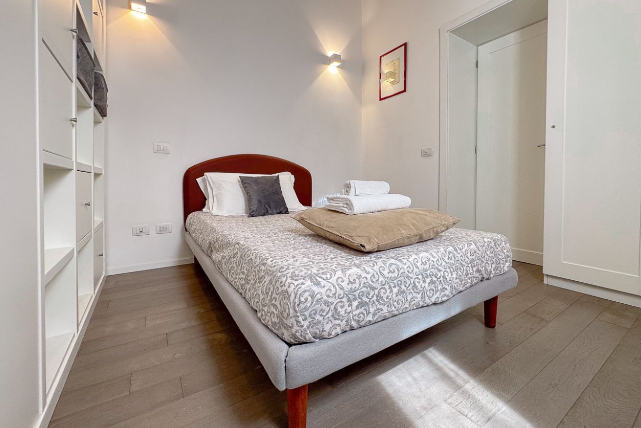 A neatly made bed with a patterned bedspread, a red headboard, and a wall-mounted light fixture.