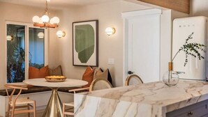 A modern kitchen with a marble countertop, a built-in oven, and a dining area with a round table and chairs. - @ Marbella Lane - Vibrant & Chic Designer Home (Fullerton)