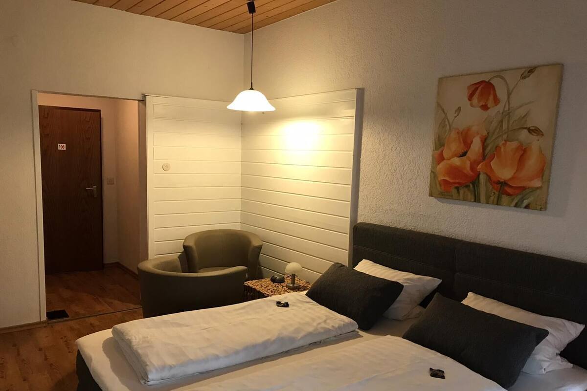 A bedroom with a bed, a chair, a desk, and a painting on the wall.