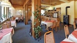 Un restaurant chaleureux, avec un décor intérieur en bois, des tables recouvertes de nappes rouges et une cuisine ouverte.