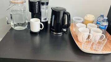A black table with a water dispenser, a coffee maker, a mug, and a tray with cups and water bottles.