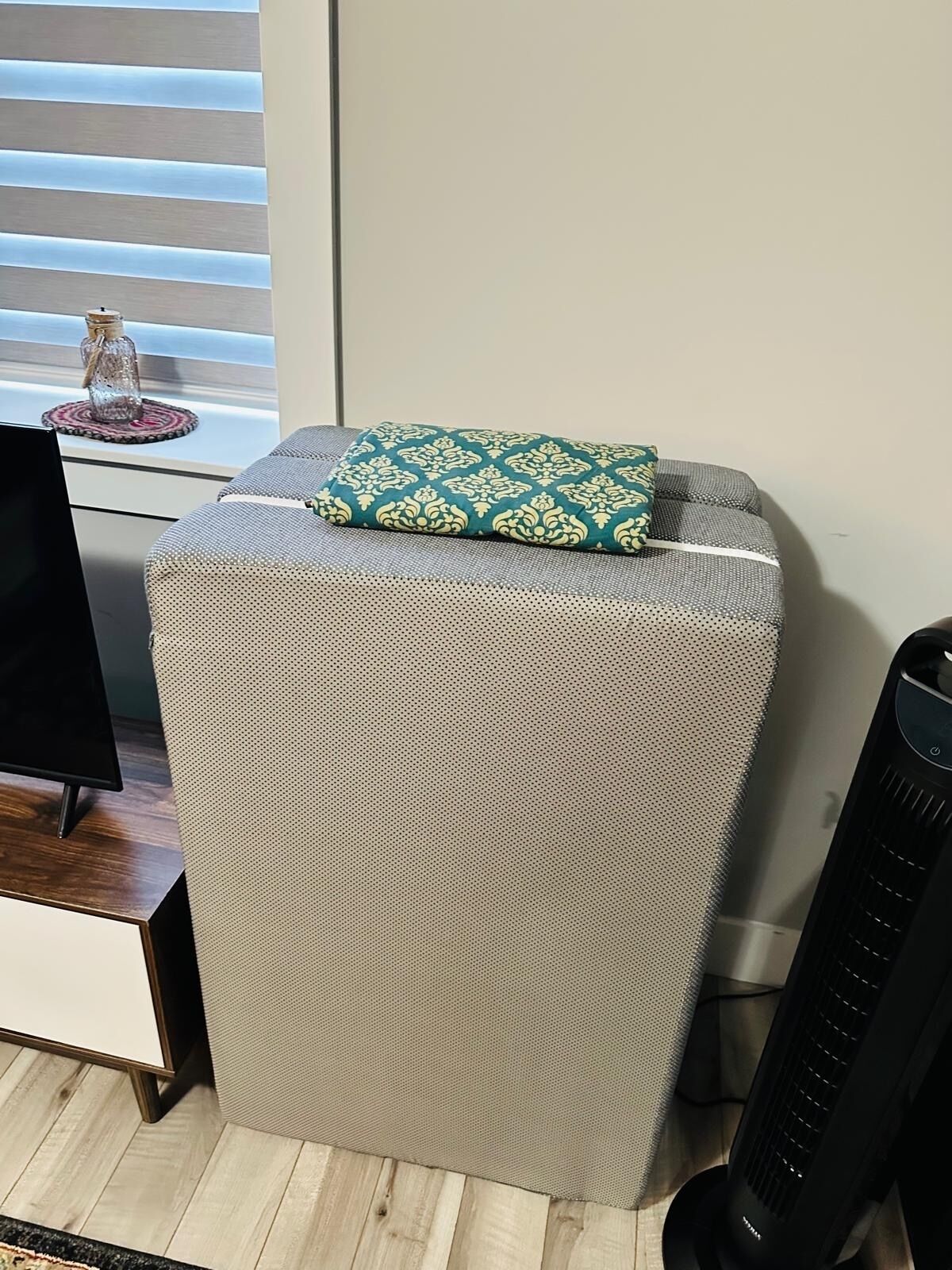 Un petit espace salon fermé, doté d’un coussin à motifs, d’un téléviseur et d’un radiateur.