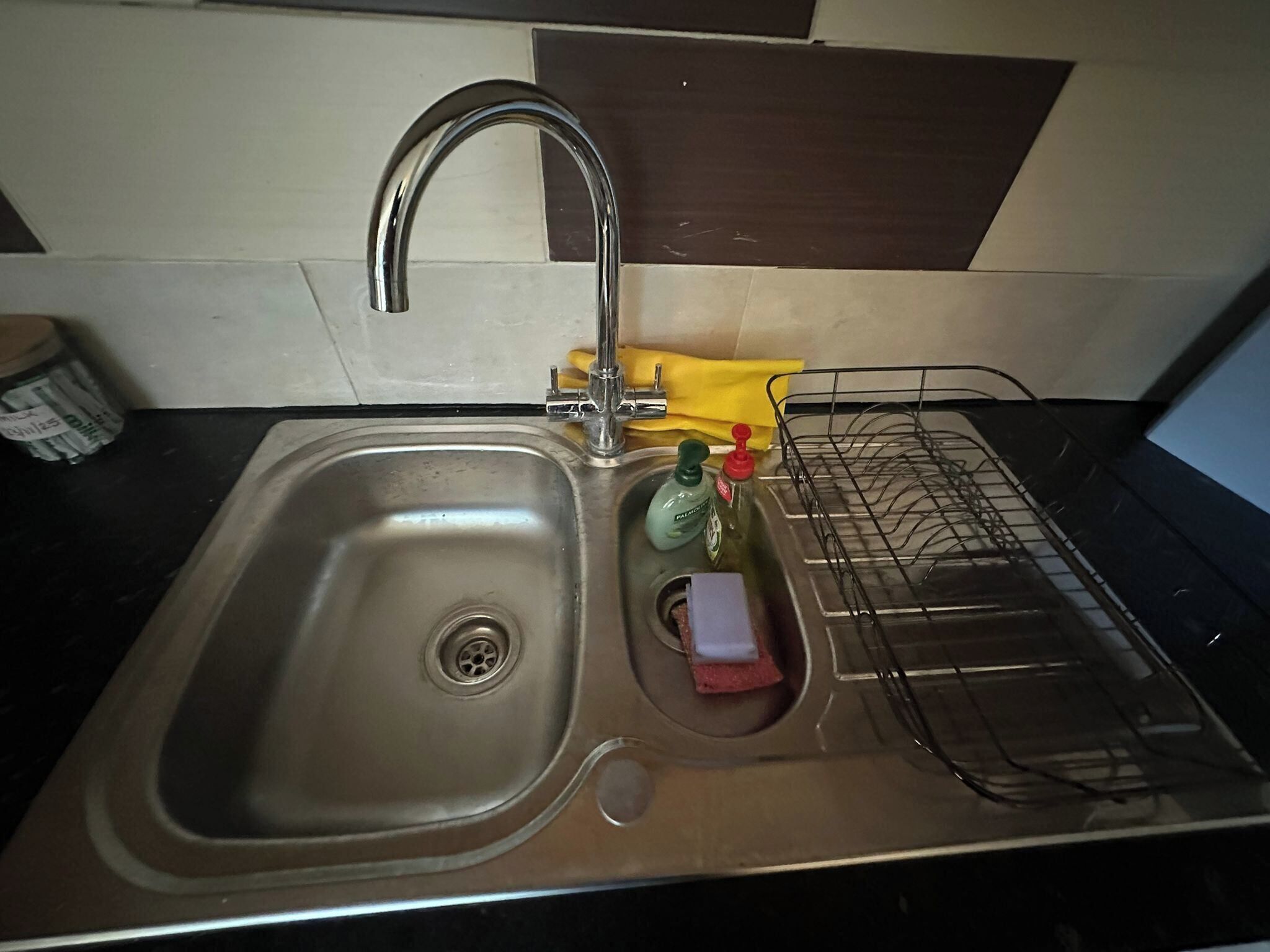 Eine Spüle mit Wasserhahn, ein Geschirrgestell und eine Flasche Spülmittel.