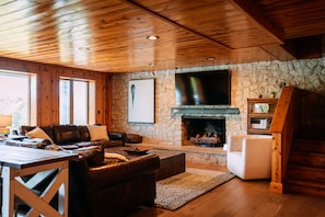 Un salon chaleureux avec une cheminée en pierre, un plafond en bois et un téléviseur fixé au mur.