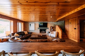 A cozy living room with a stone fireplace, wooden ceiling, and a large TV mounted above it.