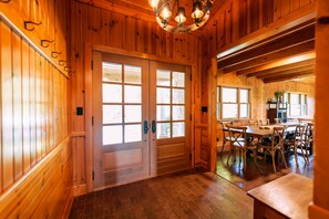 A wooden interior with a dining area, large windows, and a chandelier.