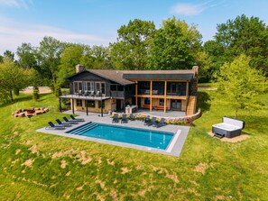 A two-story house with a swimming pool, outdoor seating, and a stone fireplace.