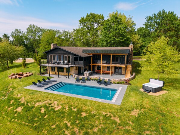 A two-story house with a swimming pool, outdoor seating, and a stone fireplace.