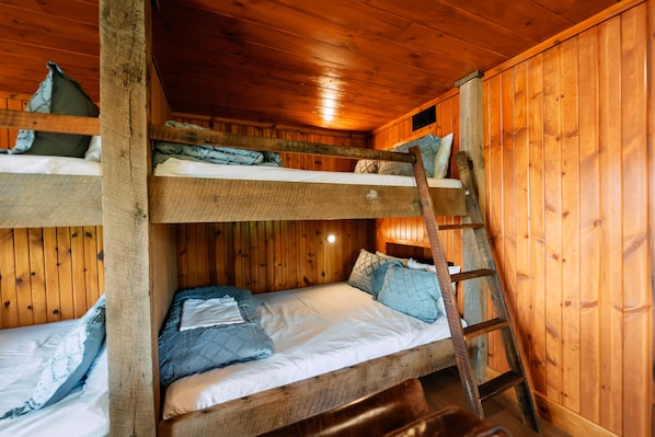 Quarto com beliches, paredes de madeira e escada.