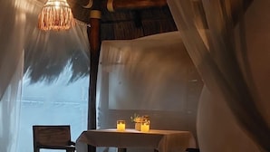 Ein gemütlicher Essbereich mit Tisch, Stühlen, einer Hängeleuchte und Kerzen auf dem Boden.