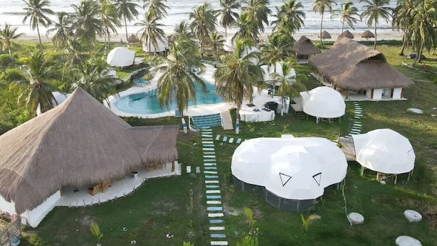 Ein Resort mit strohgedeckten Hütten, einem Swimmingpool und Palmen.