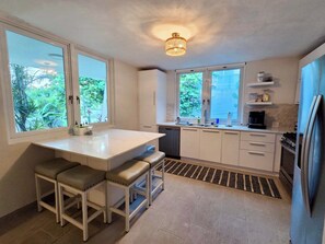 Una cocina moderna con una isla central, dos taburetes de bar, horno empotrado y ventana con vistas a zonas verdes.