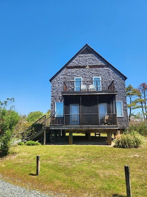 Une maison en bois à deux étages, dotée d’un balcon, d’un escalier et d’une cour gazonnée.