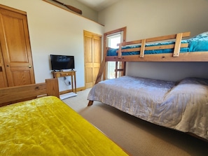 Une chambre avec un lit superposé, une télévision posée sur une petite table, une porte en bois et une fenêtre.