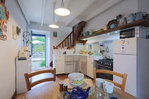 Une cuisine avec des meubles blancs, une table à manger en bois, une théière bleue et un réfrigérateur.