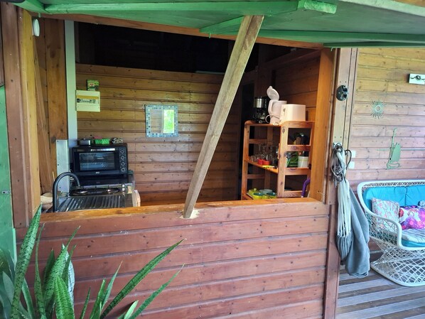 A wooden cabin interior with a kitchenette, a shelf with glassware, and a rocking chair.