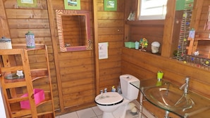 Een betegelde badkamer met een glazen wastafel, een toilet en een houten plank met toiletartikelen.