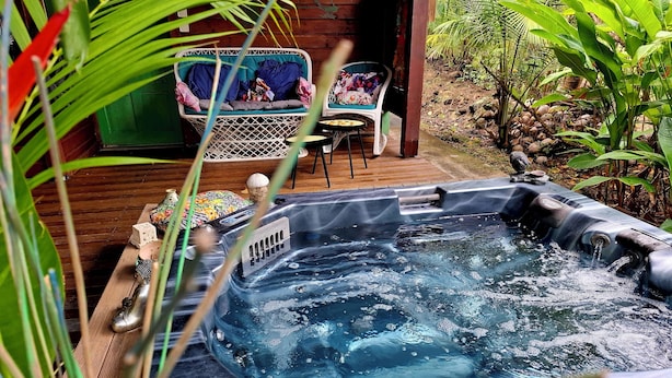 Een hottub met een houten terras, omgeven door weelderige begroeiing en een houten constructie.