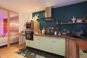 Een moderne keuken met een magnetron, oven en een rvs afzuigkap. Er is een houten aanrechtblad met diverse keukenbenodigdheden en een backsplash van hexagontegels.