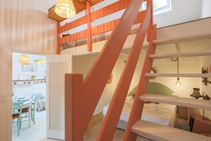 Une pièce comprenant un lit, un bureau et une chaise. Un escalier y mène à un niveau supérieur.