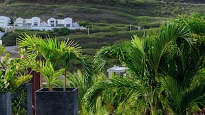 Zona de piscina con vistas a una colina verde exuberante y edificios blancos al fondo.